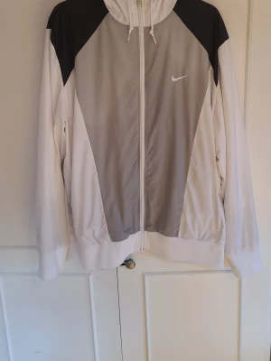 Nike vindjacka/vårjacka - En snygg vit svart nike vindjacka med luvai storlek XL, passar perfekt till våren eller hösten. Har Används väldigt fåtal gånger, har några minimala gröna fläckar på högra armen men borde utan problem gå bort i tvätt