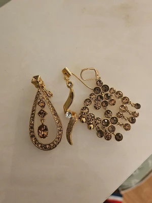Guldiga statementörhängen med stenar - Två olika guldiga örhängen med gnistrande bruna och klara stenar. Ena örhänget har droppform med hängande sten, det andra har en unik design med flera små cirklar och stenar. Perfekta för dig som gillar att sticka ut och vill ha något annorlunda.