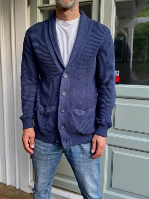 Mörkblå ribbstickad kofta - Snygg mörkblå ribbstickad kofta/cardigan. Perfekt att slänga över en t-shirt för en avslappnad känsla. Tröjan är från märket reserved och är i storlek S men är något större i storleken. Modellen är 180cm lång och väger cirka 70kg