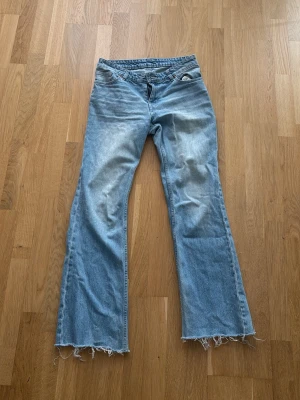 Ljusblå jeans från mobil - Snygga ljusblå bootcut jeans med trendigt råa och fransiga benslut. Klassisk femficksmodell i denim med normal midja. Perfekta för en avslappnad och cool stil.