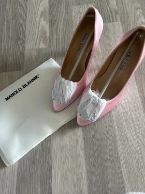 Hangisi Rosa pumps  - Snygga rosa pumps hangisi i satin med spetsig tå och låg klack. Skorna har en elegant rosett framtill och klassisk siluett. Perfekta för dig som vill ha en lyxig och feminin touch till din outfit.