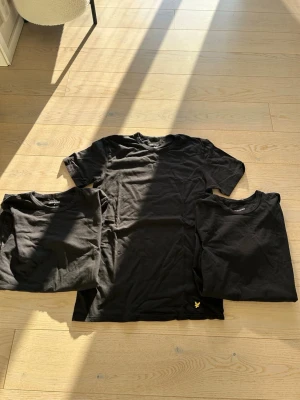 3 pack t-shirt från Lyle & Scott - Klassisk 3 pack svarta t-shirtar från Lyle & Scott med rund hals och korta ärmar. Diskret gul logga broderad längst ner på vänstra sidan. Perfekt basic-plagg med normal passform och mjukt bomullsmaterial. Är skrynkliga men är faktiskt aldrig använda pågrund av förstora 
