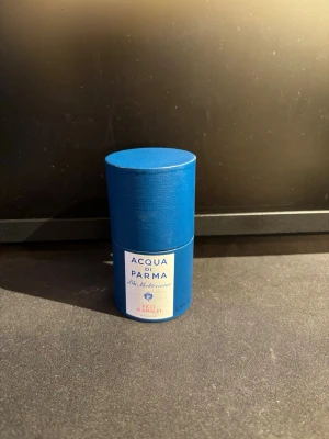 Acqua di Parma Blu Mediterraneo Fico di Amalfi - Acqua di Parma Blu Mediterraneo Fico di Amalfi är en parfym i en elegant blå cylinderformad förpackning. Märket och doftnamnet står tydligt på etiketten. Förpackningen är gjord av hård kartong och har en lyxig känsla med sin djupblå färg och vita etikett.