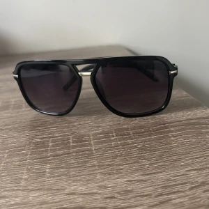 Svarta pilotbågar solglasögon - Snygga solglasögon med svarta pilotbågar och mörka glas. Raka skalmar med silverfärgade detaljer vid gångjärnen och näsbryggan. Perfekt accessoar för en cool look i sommar. Köpts för 1150kt