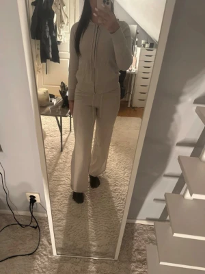 Beige mjukis-set med dragkedja - Säljer ett beige loungewear-set med ziptröja och matchande byxor. Tröjan har huva och dragkedja framtill, byxorna har raka ben och resår i midjan. Perfekt för chill dagar hemma eller när du vill vara extra bekväm.