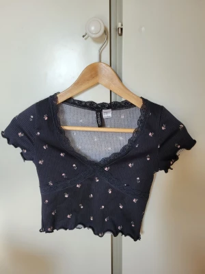 Svart croppad topp från H&M Divided - Söt svart croppad topp från H&M Divided med små blommor, spetskant vid v-ringningen.
