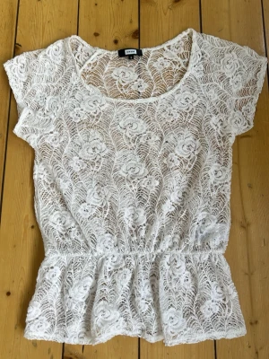 Vit spetsblus med blommönster - Säljer en superfin vit spetsblus från Bik Bok med blommigt mönster. Blusen har korta ärmar, rund halsringning och resår i midjan för en snygg passform. Perfekt att styla över ett linne eller bh för en trendig look.