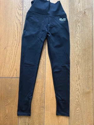 Svarta leggings från EVE Paris - Snygga svarta tights från EVE Peach med hög midja och diskret logga på vänster höft. Rosett knyts baktill. Tillverkade i stretchigt material (se bild) som sitter tight och bekvämt. Scrunch baktill. Perfekta för en trendig och sportig look. Aldrig använda, endast provade. Säljes pga de inte passade mig.