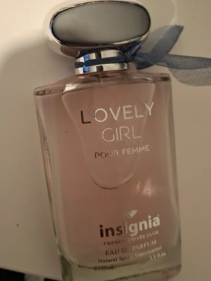 Lovely Girl parfym från Insignia - Säljer en Lovely Girl pour femme parfym från Insignia. Flaskan är rektangulär i genomskinligt glas med ljusrosa doftvätska och har ett silverfärgat lock samt en blå rosett runt halsen. Snygg och stilren design som passar perfekt på sminkbordet.