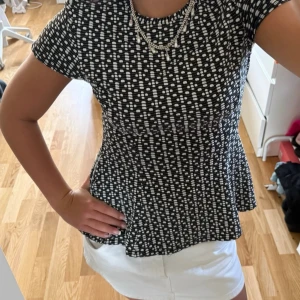 Svartvit prickig topp med peplum - Säljer en svartvit topp med prickigt mönster och peplumformad midja. Toppen har rund halsringning och korta ärmar. Materialet känns stretchigt och bekvämt, perfekt för en trendig vardagslook.