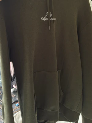 Olivgrön hoodie från Polo Ralph Lauren - Snygg olivgrön hoodie från Polo Ralph Lauren med broderad logga på bröstet. Klassisk känguruficka framtill och justerbar huva med snören. Tillverkad i mjukt bomullsmaterial som känns skönt mot huden. Perfekt för en avslappnad och stilren look.
