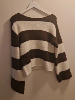 Randig stickad tröja Gina Tricot - Stickad tröja från Gina Tricot med breda horisontella ränder i brunt och vitt. Tröjan har en avslappnad passform, långa ärmar och rund halsringning. Perfekt för dig som gillar en mysig och trendig look.