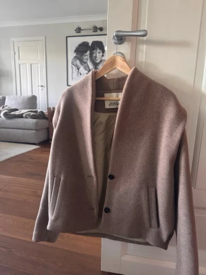Beige cardiganjacka från Isabel Marant - Snygg beige cardiganjacka från Isabel Marant med två knappar framtill och raka fickor. Jackan har en avslappnad passform, mjukt ullmaterial och är helfodrad på insidan. Perfekt för lager på lager och en stilren look.