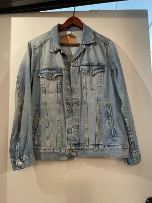 Ljusblå klassisk jeansjacka - Snygg ljusblå jeansjacka med raka sömmar och två bröstfickor med lock och knapp. Jackan har silverfärgade knappar framtill och två sidofickor. Perfekt oversized passform och tidlös design som funkar till allt.