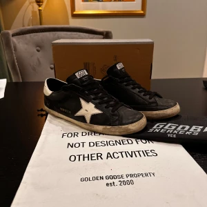 Svarta sneakers från Golden Goose - Säljer ett par svarta Golden Goose sneakers i bra skick. Slitna detaljer. Skorna har snörning och är perfekta för en avslappnad stil. Innersulan är mjuk och bekväm, vilket gör dem sköna att ha på sig hela dagen. Pris går att diskutera!