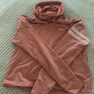 Tränings hoodie från Stronger - Fin orange/korall hoodie från Stronger med krage och snörning. Tyvärr blivit för liten för mig därav jag säljer💕Nytt pris 799 kr, säljer för 179 kr (pris kan alltid diskuteras)!! Bara att skriva vid frågor eller fler bilder💕