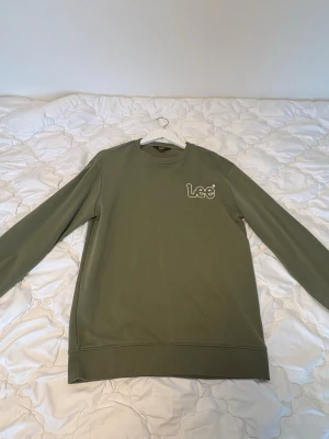 Olivgrön sweatshirt från Lee - Snygg olivgrön sweatshirt från Lee med rund halsringning och diskret logga broderad på bröstet. Tröjan har långa ärmar och ribbade muddar vid ärmslut och nederkant. Perfekt för en avslappnad och stilren look.