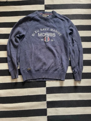 Blå tröja från Morris med tryck - Snygg blå tröja från Morris med texten 'Bleu Navy Marine' och ett tryck framtill. Tröjan har rund halsringning, ribbade muddar och nederkant. Perfekt för dig som gillar klassisk och sportig stil. Storlek S.