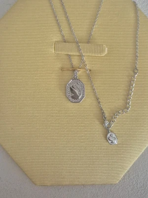 Silverhalsband Swarovski - Rodium platerad. Rodium är en mycket sällsynt, korrosionsbeständig ädelmetall som främst används i bilkatalysatorer och smycken. Dess begränsade tillgång gör den till en av världens dyraste metaller.Ett Swarovski-halsband med svanmotiv och pavéinfattade kristaller. Rhodiumpläterad metall (Swarovski använder ofta rhodiumplätering på sina silverfärgade smycken).