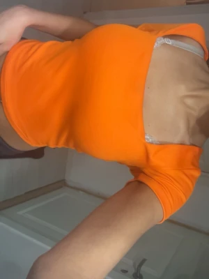 Orange croppad topp med fyrkantig ringning - Snygg orange croppad topp med fyrkantig ringning och korta ärmar. Toppen har en tight passform och är tillverkad i ett stretchigt material som sitter skönt mot kroppen. Perfekt för dig som vill sticka ut med en färgstark look.