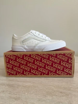 Vita Vans sneakers i läder - Snygga vita sneakers från Vans i texturerat läder med klassisk låg siluett. Skorna har vita snören, diskret Vans-logga på sidan och en stilren design som passar till det mesta. Perfekta för dig som gillar enkel men trendig stil.