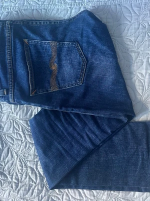 Blå jeans från Nudie Jeans - Snygga blå jeans från Nudie Jeans med klassisk femficksmodell och gul kontrastsöm på bakfickan. Jeansen har en rak passform och är tillverkade i mjuk denim. Perfekta för dig som gillar stilrena och tidlösa jeans.