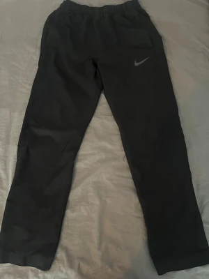 Svarta dri-tech byxor från Nike - Svarta dri-tech från Nike med klassisk logga på vänster lår. Byxorna har rak passform, resår i midjan och är tillverkade i ett mjukt material som passar perfekt för chill eller träning. Snygg och enkel design som funkar till det mesta.
