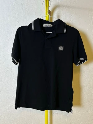 Svart piké från Stone Island - Denna vara kommer att auktioneras ut på Plick Live den 3 juni klockan 19:00