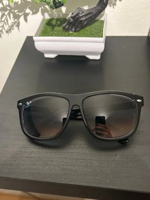 Ray-Ban Boyfriend  - Klassiska svarta Ray-Ban Wayfarer solglasögon med bred båge och mörka glas. Snygg och tidlös design med Ray-Ban-logga på sidan. Perfekta för soliga dagar och ger en cool vibe till din outfit.