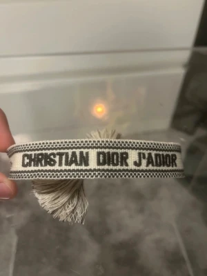 Christian Dior armband - Snyggt armband från Christian Dior. Armbandet är vävt i tyg och har dekorativa tofsar i ändarna. Perfekt accessoar för att lyfta din outfit till sommarn!