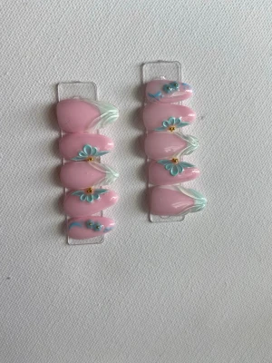 Press-on naglar rosa med stenar - Snygga press-on naglar i rosa med blå detaljer och glittrande stenar. Naglarna har en oval form och är dekorerade med 3D-effekter för en trendig look. Perfekt för dig som vill ha något extra till naglarna.