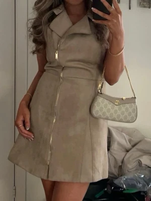 Beige mockaklänning med dragkedja - Snygg beige klänning i mocka-look med markerad krage och dragkedja framtill. 