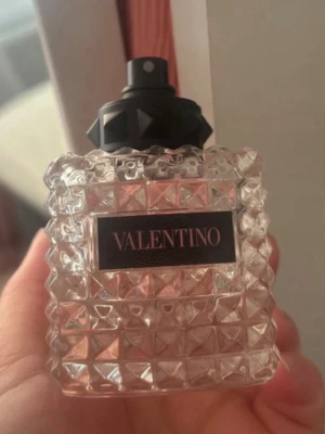 Valentino parfym med nitar - Säljer en lyxig parfym från Valentino i en transparent glasflaska med nitar och rutmönster. Flaskan har svart spraykork med coola detaljer och en elegant etikett framtill. Perfekt för dig som gillar exklusiva dofter och snygg design.ca 7 ml kvar perfekt för dem som vill prova innan de köper😊