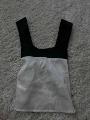 Svartvit linnetopp med breda axelband - Snygg svartvit linnetopp med breda axelband och rak skärning. Toppen har svart överdel och vit nederdel, vilket ger en stilren kontrast. Perfekt att matcha med jeans eller kjol för en trendig look.