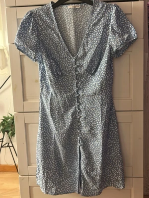 Blå mönstrad kortklänning - Säljer en blå kortklänning med v-ringning, korta puffärmar och knappar framtill. Materialet känns lätt och bekvämt. I nyskick🩵