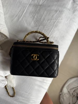 Svart quiltad handväska från Chanel - Jag kan minska priset 😊även kan mötas i stockholm . Säljer en svart quiltad handväska från Chanel med guldfärgade detaljer och kedjerem. Väskan har det klassiska CC-spännet framtill, dragkedja upptill och ett litet handtag. Insidan har spegel och kortfack. Perfekt för dig som gillar lyxiga accessoarer.