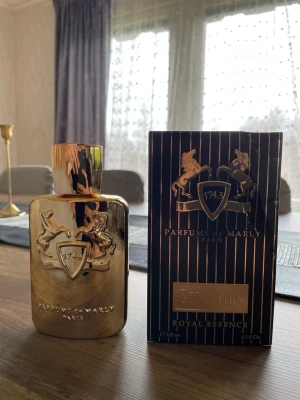 Parfums de Marly Godolphin EdP 125ml - Lyxig parfym från Parfums de Marly, modellen Godolphin. Flaskan är i metalliskt guld med relief av två hästar och en sköld med siffran 1743. Förpackningen är svart med guldiga detaljer och text. Innehåller 125 ml Eau de Parfum.