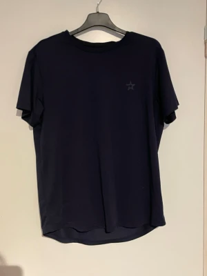 Mörkblå t-shirt med stjärndetalj - En stilren mörkblå t-shirt med en liten stjärna tryckt på bröstet. T-shirten har rund halsringning och korta ärmar, perfekt för en clean och enkel look. Passar dig som gillar minimalistisk stil.