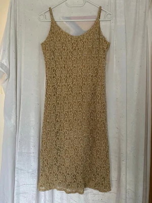 Beige spetsklänning med smala band - Snygg beige klänning med smala axelband och v-ringning. Klänningen är täckt av ett vackert spetsmönster med insydda pärlor och har en kort längd som passar perfekt till sommaren.