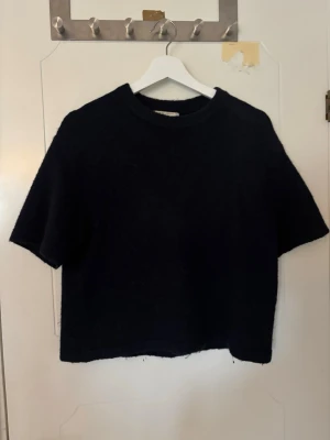 Svart stickad tröja Gina Tricot - Trendig kortärmad svart stickad tröja från Gina Tricot i premiumkvalitet. Tröjan är gjord i ett mjukt, fluffigt material. Perfekt för lager på lager och enkel att styla till olika looks. 