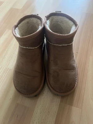 Beige/Bruna fodrade boots från 157 - Säljer ett par bruna boots från 157 med mjukt, vitt foder på insidan. Skorna har en rund tå och är tillverkade i mockaliknande material. Perfekta för kalla dagar och har en enkel, stilren design. Storlek 34/35