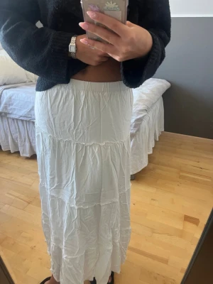 Vit långkjol från Brandy Melville - Säljer denna superfina vita långkjolen från Brandy Melville. Kjolen har flera volanger och resår i midjan. Perfekt till sommaren!!🙌🏻🌟