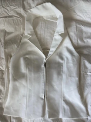 Vit figurnära väst från Zara - Snygg vit väst från Zara med figurnära passform och markerad krage. Västen har dragkedja framtill och stilrena sömmar som ger en skräddad look. Perfekt att styla över en topp eller skjorta för en trendig vibe.