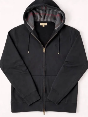 Svart hoodie med dragkedja Burberry - Svart hoodie från Burberry med hel dragkedja och klassiskt rutmönster i huvan. Mjukt material, justerbar huva med snören och två fickor framtill. Perfekt för en stilren och avslappnad look.Skriv vid fler frågor.Äkta kvitto finns !