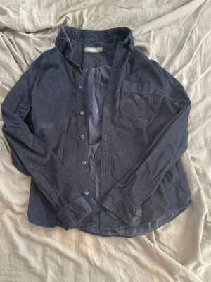 Mörkblå skjorta i bomull - Snygg mörkblå manchester skjorta från Dressmann. Klassisk krage, bröstficka och knappar framtill. Perfekt för en avslappnad men stilren look. Långärmad och i normal passform.