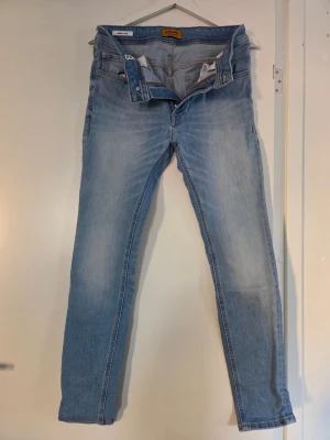 Ljusblå skinny jeans från Jack & Jones - Ljusblå skinny jeans från Jack & Jones med klassisk femficksdesign och orangea sömmar. Jeansen är tillverkade i denim och har en modern passform som sitter tight längs benen. Perfekt för dig som gillar en avslappnad och trendig look.