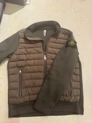 STONE ISLAND CARDIGAN  - Snygg grön cardiganjacka från Stone Island med quiltad front och släta ärmar. Jackan har två dragkedjefickor fram, ribbade muddar och klassisk Stone Island patch på vänster ärm. Materialmix med vadderad front och mjuka ärmar ger en modern look. /ge gärna bud 