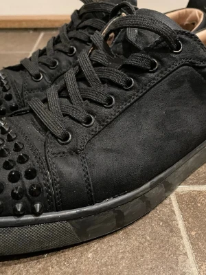  Louboutin skor - Säljer ett par svarta sneakers från Christian Louboutin med nitar. Bortsett från skadorna på insidan och fläcken man ser på bild 5 är de i bra skick, fläcken är dock inte så synlig när man har på sig dem. Tvättar innan jag skickar. Tveka inte på att höra av dig vid frågor😁