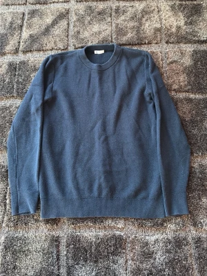 Mörkblå stickad tröja med rund hals - En enkel och stilren mörkblå stickad tröja med rund halsringning och långa ärmar. Tröjan har ribbstickade muddar vid ärmslut och nederkant. Perfekt för lager-på-lager och passar till jeans eller chinos.