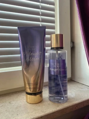 Victoria's Secret Midnight Bloom set - Säljer ett set med Victoria's Secret Midnight Bloom, innehållande en body mist och en lotion. Båda har en snygg lila och guldig design med genomskinliga och metalliska detaljer. Doften är blommig och fräsch, perfekt för dig som gillar feminina parfymer.